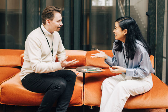 Businessman discussing with happy female colleague while sitting on sofa in congress center