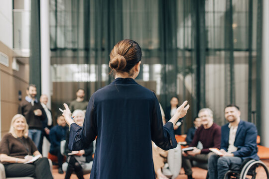 Rear view of female delegate explaining strategies while giving lecture at summit to business people at congress center