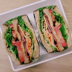 A delicious sandwich featuring layers of lettuce, tomato, bacon, and various meats, served in a container for a tasty meal option.