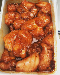 Marinated chicken pieces in a container, displaying rich hues of spice and sauce, ready for cooking or grilling.