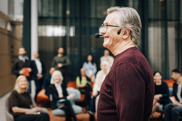 Side view of smiling senior male keynote speaker giving lecture at business seminar in congress center
