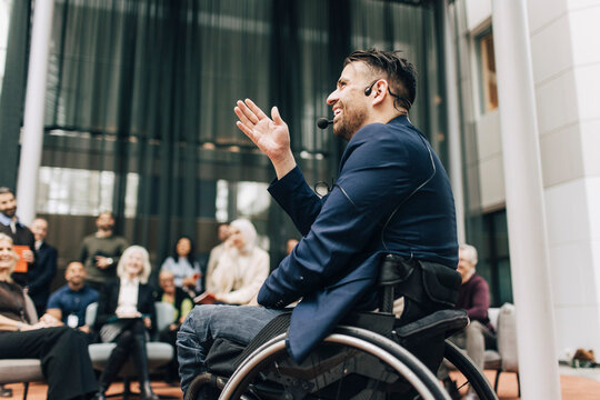 Low angle view of smiling physically disabled male delegate wearing headset giving lecture at business summit in congres