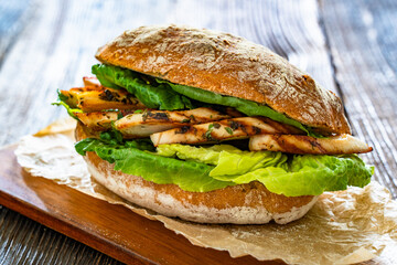 Takeaway sandwich with slices of grilled chicken breast on wooden table	
