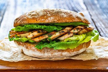 Takeaway sandwich with slices of grilled chicken breast on wooden table	
