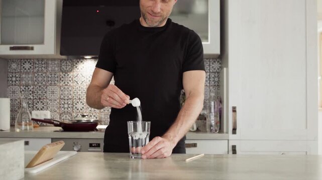 4K close-up young fit male preparing protein shake in kitchen, pouring creatine powder into glass, healthy nutrition for muscle growth, fitness lifestyle, sport training and bodybuilding concept