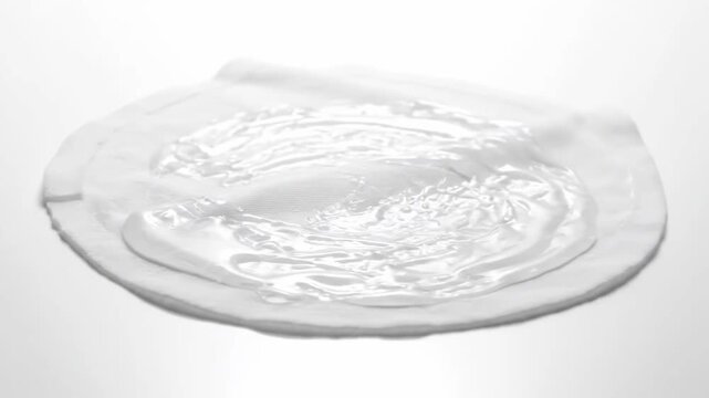Gel on Fabric Pad - A close-up shot reveals a white, circular fabric pad with a clear gel substance spread across its surface. The gel has a slightly textured, uneven appearance.