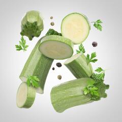 Pieces of fresh zucchinis, parsley and peppercorns falling on light grey gradient background
