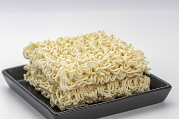 Uncooked instant noodle block on black plate raw ramen square dry wavy pasta beige color simple food minimal style studio light clean background comfort mood close up