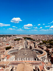 Petersplatz mit Blick auf Rom bei strahlend blauem Himmel.
Panoramablick &uuml;ber den Petersplatz in Rom mit Obelisk, Kolonnaden und weitem Stadtpanorama unter blauem Himmel mit Wolken.