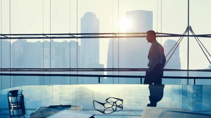 Silhouette of a man gazing at a cityscape through a large window. Low-angle shot, evoking a contemplative, cinematic video feel. Live desktop wallpaper. - Powered by Adobe