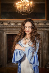 Beautiful sensual woman wears vintage underwear stands in the medieval room of the old castle with old-fashioned chandelier