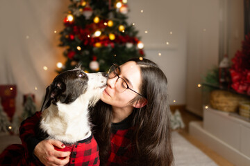 Puppy dog kissing her owner woman celebrating christmas and wearing red pajamas