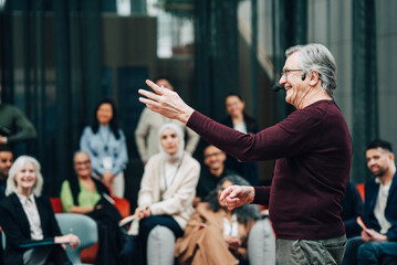 Happy male keynote speaker wearing headset gesturing while giving lecture at summit in convention center