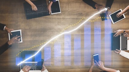 A top-down view of a diverse group of professionals engaged in a business meeting, utilizing digital devices and showcasing a growth chart for strategic planning. Copula