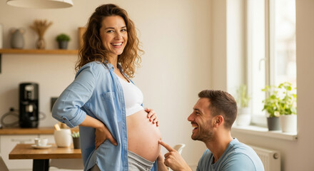 Fototapeta premium Pregnant woman with partner in blue shirt at kitchen touching belly. Happy couple maternity moment for prenatal wellness and home lifestyle content