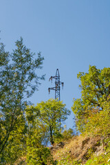 Obraz premium Electricity transmission tower rising above forest trees under clear blue sky in mountain landscape