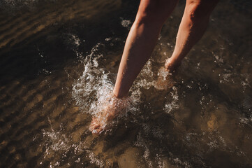 Young barefoot woman walking on water in sea in summer with splashes. Photo, close-up portrait.