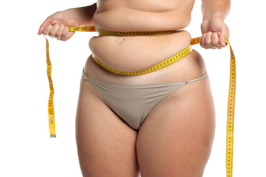Studio shot of obese woman squeezing waist fat with tape measure for weight loss and body measurement on white background.