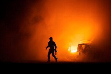 Obraz premium Silhouette of a person walking away from a burning vehicle amidst orange flames and smoke filled air
