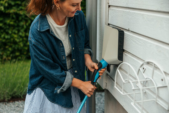 Smiling woman plugging electric plug in outlet on outside wall in back yard