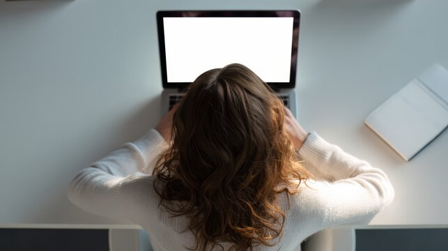 Woman is sitting at a desk with a laptop open in front of her. She is focused on her work