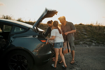 Family unloading car trunk at picnic spot against clear sky