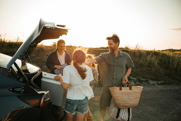 Family unloading things from car trunk at picnic spot against clear sky