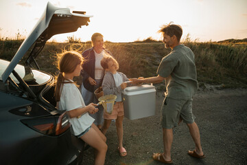 Sisters helping their parents in unloading car trunk at picnic spot