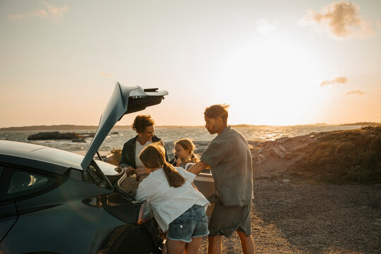 Family members unloading car trunk near sea shore against sky