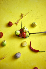 Fresh vegetables and quail eggs on a bright yellow background. Brussels sprouts, chili peppers, and tomatoes arranged creatively for healthy food and culinary concepts