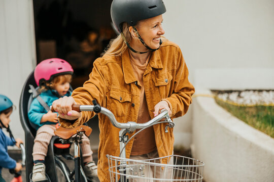 Smiling woman wheeling bicycle with kids in background