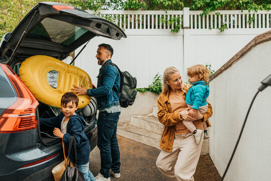 Family preparing for weekend trip while loading luggage in car trunk