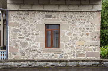 Old stone wall pattern texture or background. Backdrop of stone rock fence floor textured exterior surface. Exterior view and wooden front window of beautiful stone cottage house on street in village