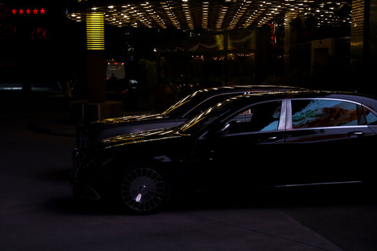 BATUMI, GEORGIA - MAY 12, 2024: dark blue Mercedes-Benz Maybach Rolls Royce car parked in the city centre near night casino Eclipse. Night city luxury life Reflection light on windows