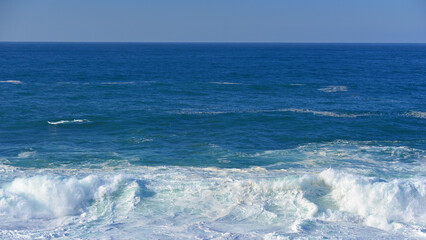The immensity of the ocean and waves of white foam on the shore.
