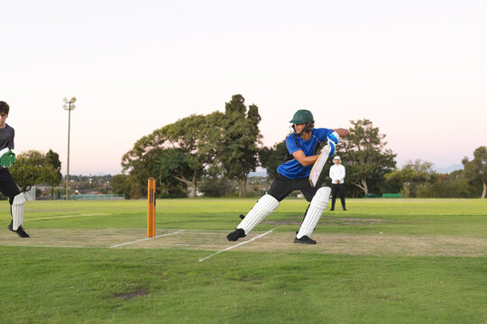 Teenage batsman in blue shirt leaning playing shot with cricket bat on grass pitch, copy space
