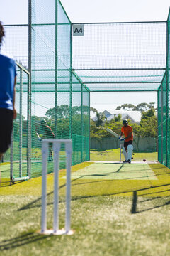 Indian male batsman in helmet holding cricket bat inside practice nets on turf with stumps