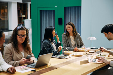 Happy female corporate employees enjoying lunch break while sitting at table in office cafeteria