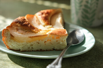 Close-up of warm homemade pie made of cottage cheese and pears on plate. Mug on blurred background and soft natural light create cozy, inviting atmosphere. Perfect for food and lifestyle content