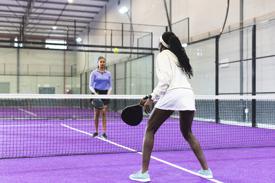 Diverse female opponents rallying with paddles at net on court chasing ball, copy space