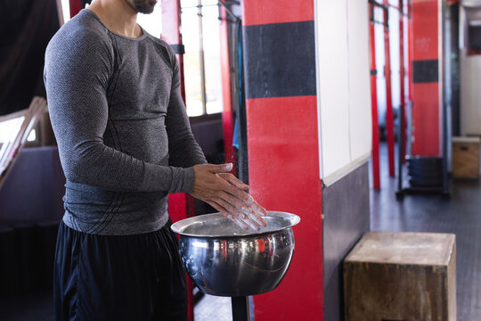 Man rubbing chalk into hands over chalk bowl in gym with pull-up rig, copy space