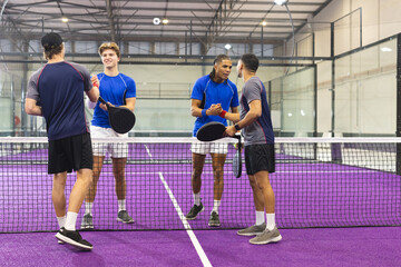 Male athletes exchanging handshakes at net on purple paddle court with rackets