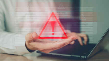 Red alert triangle icon over hand and laptop, indicating a system error, security warning, or cyber threat notification.