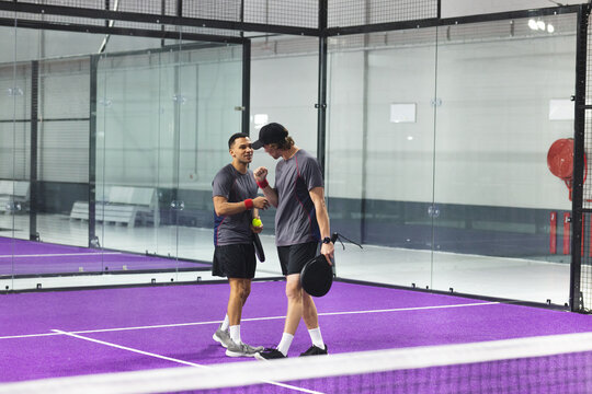 Two male padel players celebrating point on purple padel court with rackets, balls