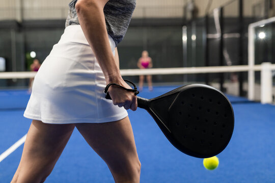 Female in white skirt swinging black paddle racket at yellow ball on blue court, copy space
