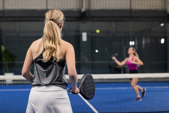 Female players in sportswear playing padel at net on blue court, holding rackets, receiving ball