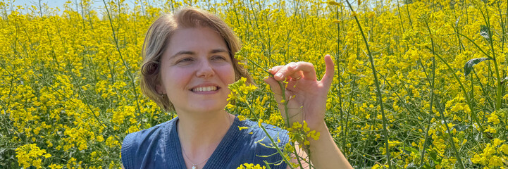 A smiling Caucasian woman admires mustard blooms, celebrating Earth Day's botanical wonders and the...