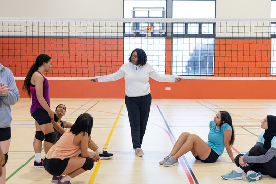 African american coach holding net on court under basketball hoop players listening in knee pads