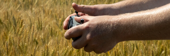 Sunlit hands clutching a drone controller dance amidst golden barley, celebrating International...