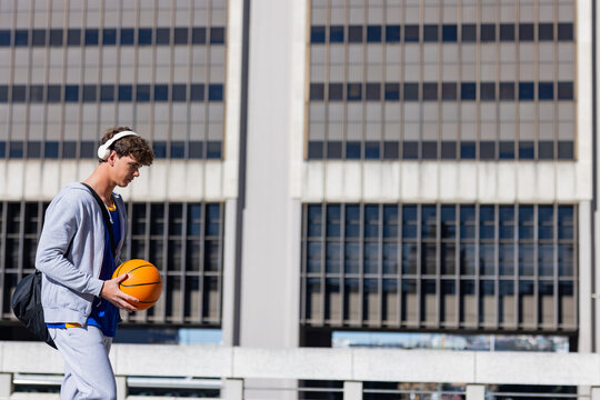 Man wearing sportswear walking on elevated walkway by building with basketball, copy space